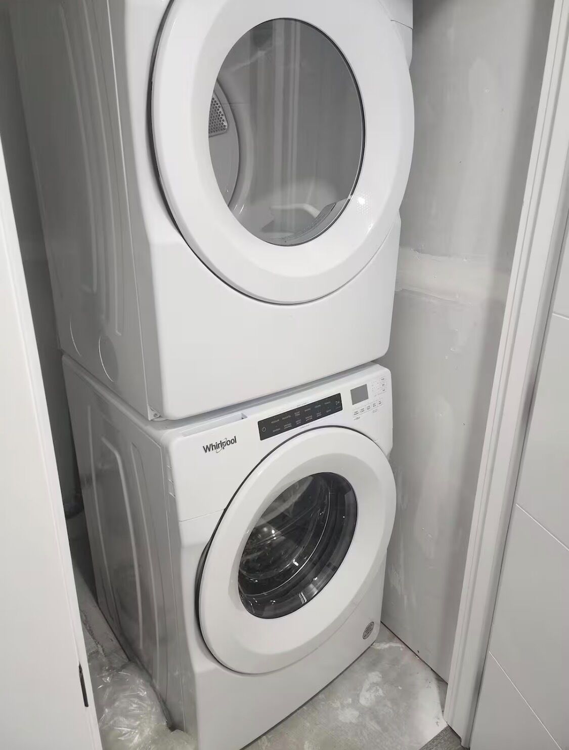 A stacked washer and dryer unit in a corner of a room.