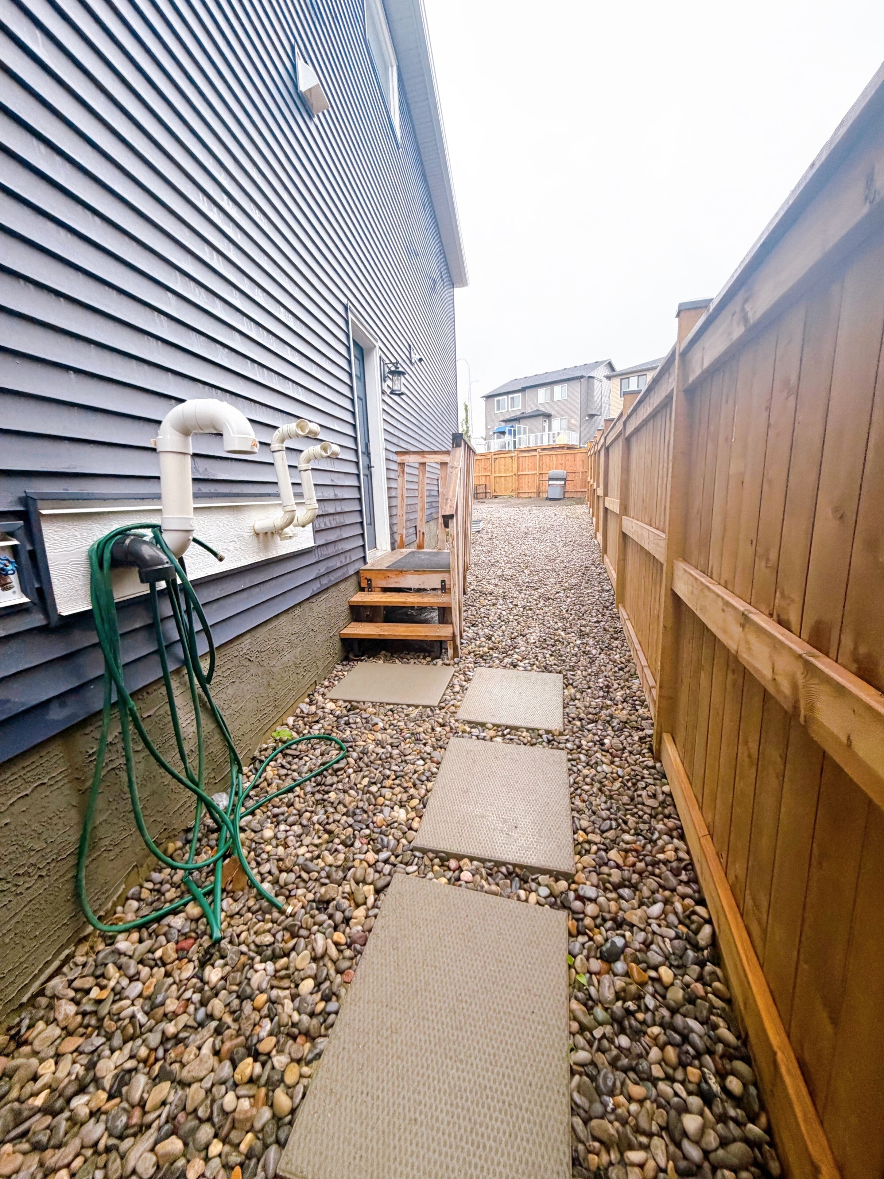 Un jardin avec une terrasse en bois, un chemin de gravier et une clôture en bois.