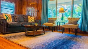 Una sala de estar con un sofá de cuero, dos sillones, una mesa de centro y un ventanal con cortinas.