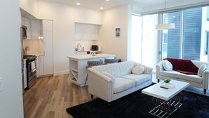 A modern living room with a white sofa, a coffee table, and a kitchen area with white cabinetry and a microwave.