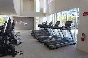 Une salle de sport équipée de tapis de course, de poids et d’un panneau indiquant : « PARK 12 THE COLLEGE ».