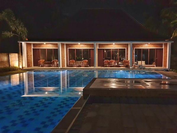 A swimming pool with a tiled deck, surrounded by a building with multiple windows and doors, and outdoor seating. - The Nalaya Hotel & Resto (Borobudur)