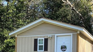 A small, single-story building with a front door, a small window, and a wooden staircase leading up to the entrance.