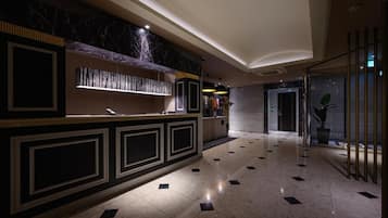 A hotel lobby with a reception desk, marble flooring, and a modern interior design.