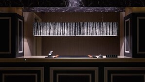 Un comptoir d’accueil avec un plateau en marbre, un panneau lumineux vertical et une enseigne indiquant « ENTRÉE ».