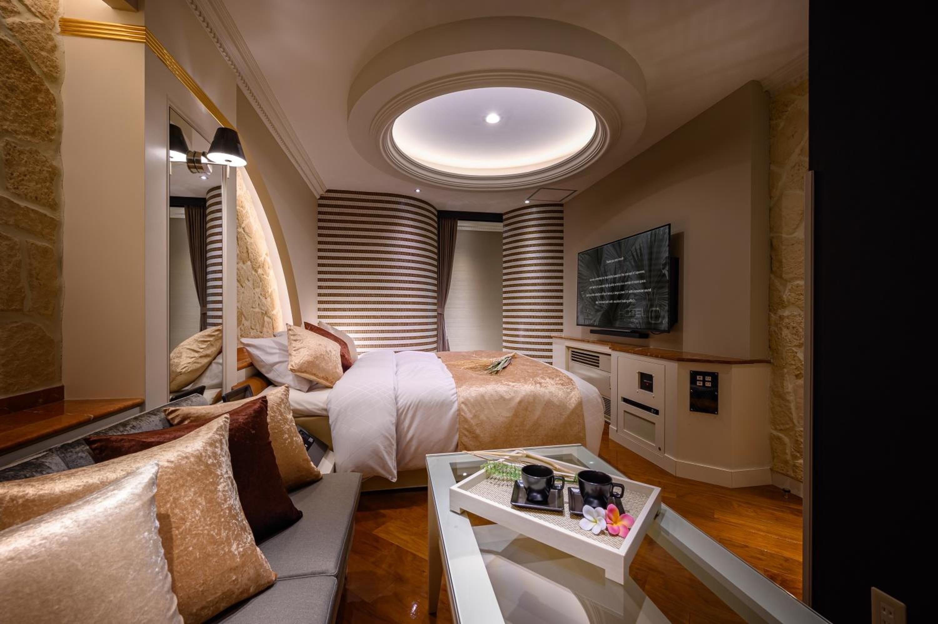 A hotel room with a bed, a sofa, a TV, a coffee table, and a ceiling light.