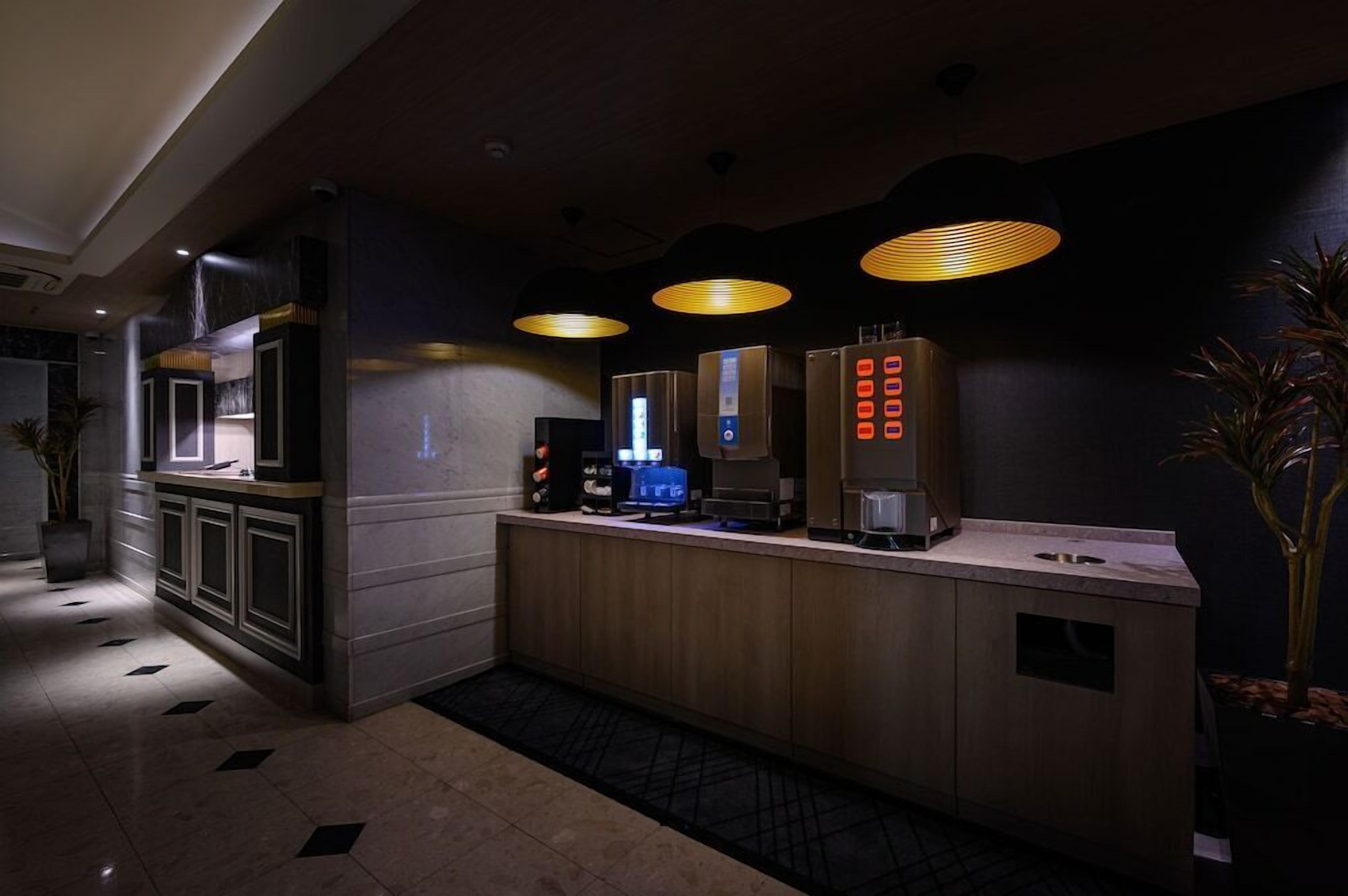 A modern hotel lobby with a reception desk, a coffee machine, and a digital display.