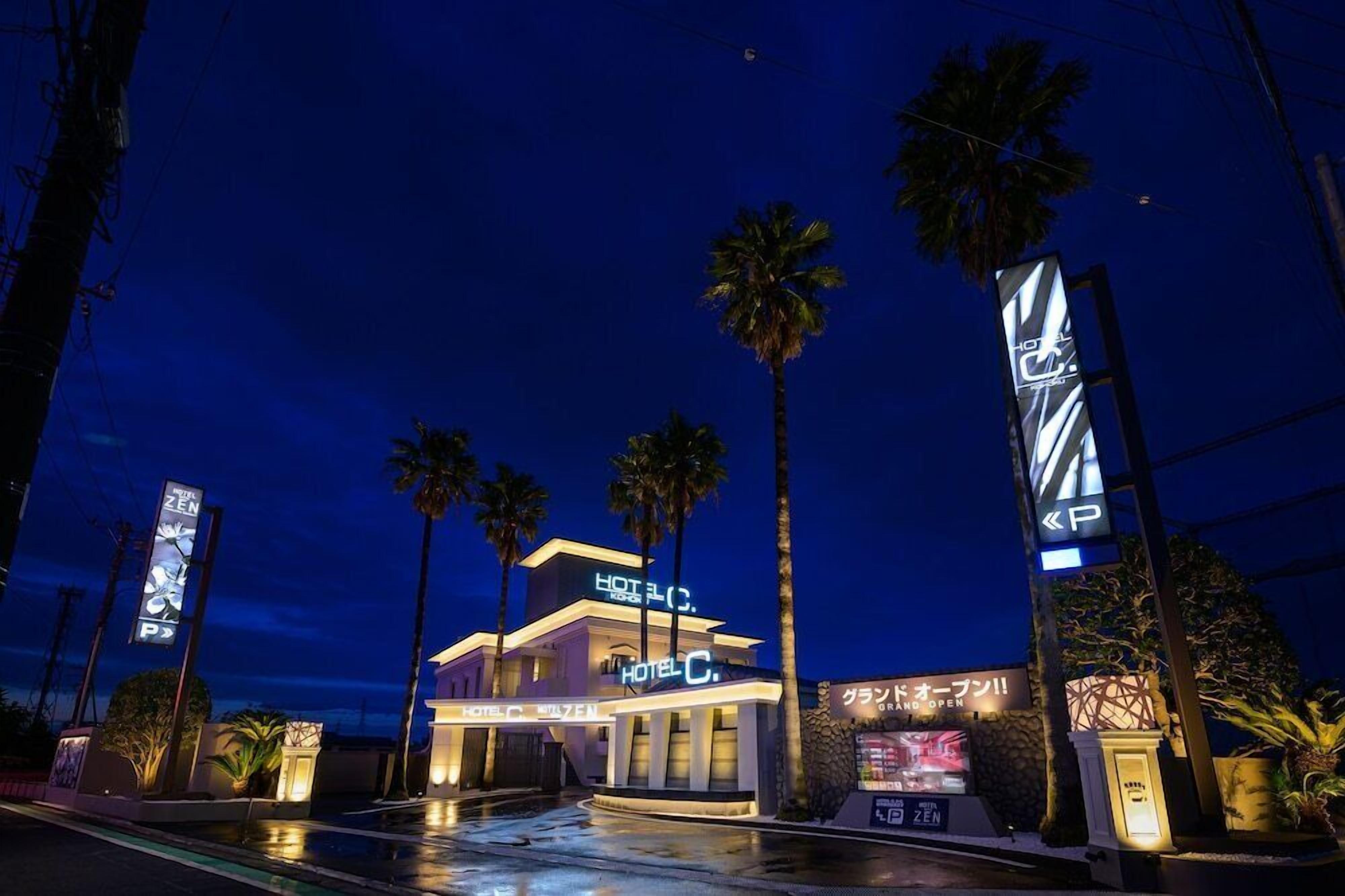 A hotel with a modern design, palm trees, and illuminated signage.