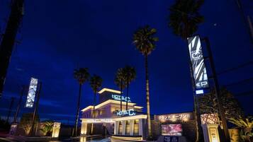 A hotel with a modern design, palm trees, and illuminated signage.