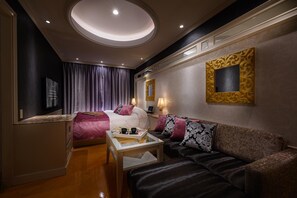 A hotel room with a bed, a sofa, a small table, a mirror, and a wall-mounted artwork. - Hotel C.kohoku (Nishitokyo)