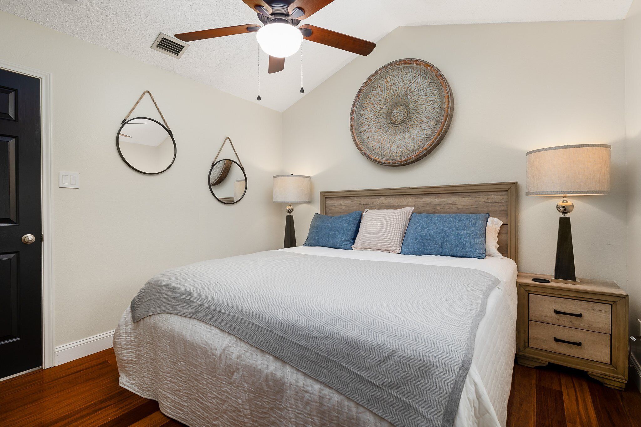 Un dormitorio con cama, lámparas de noche, ventilador de techo y decoración en las paredes.