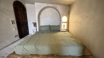 A room with a bed, a wooden door, and a wall-mounted light fixture.