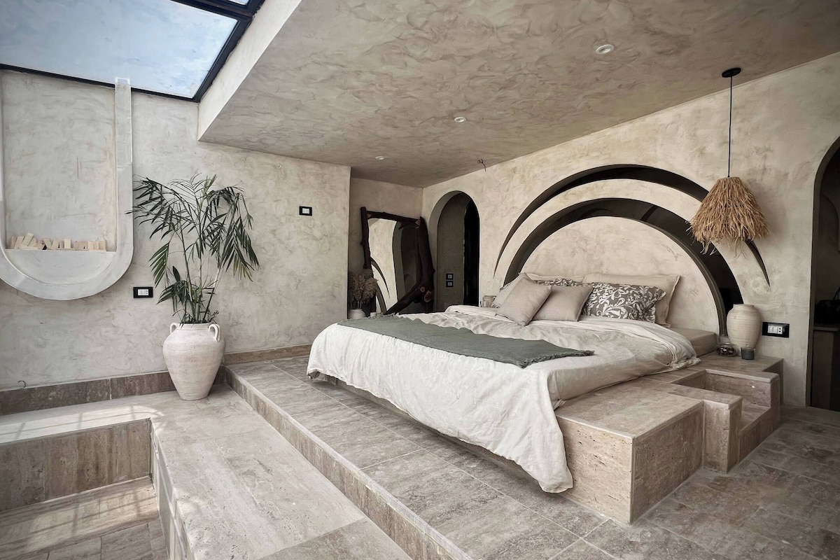 A bedroom with a large bed, a potted plant, and a skylight.