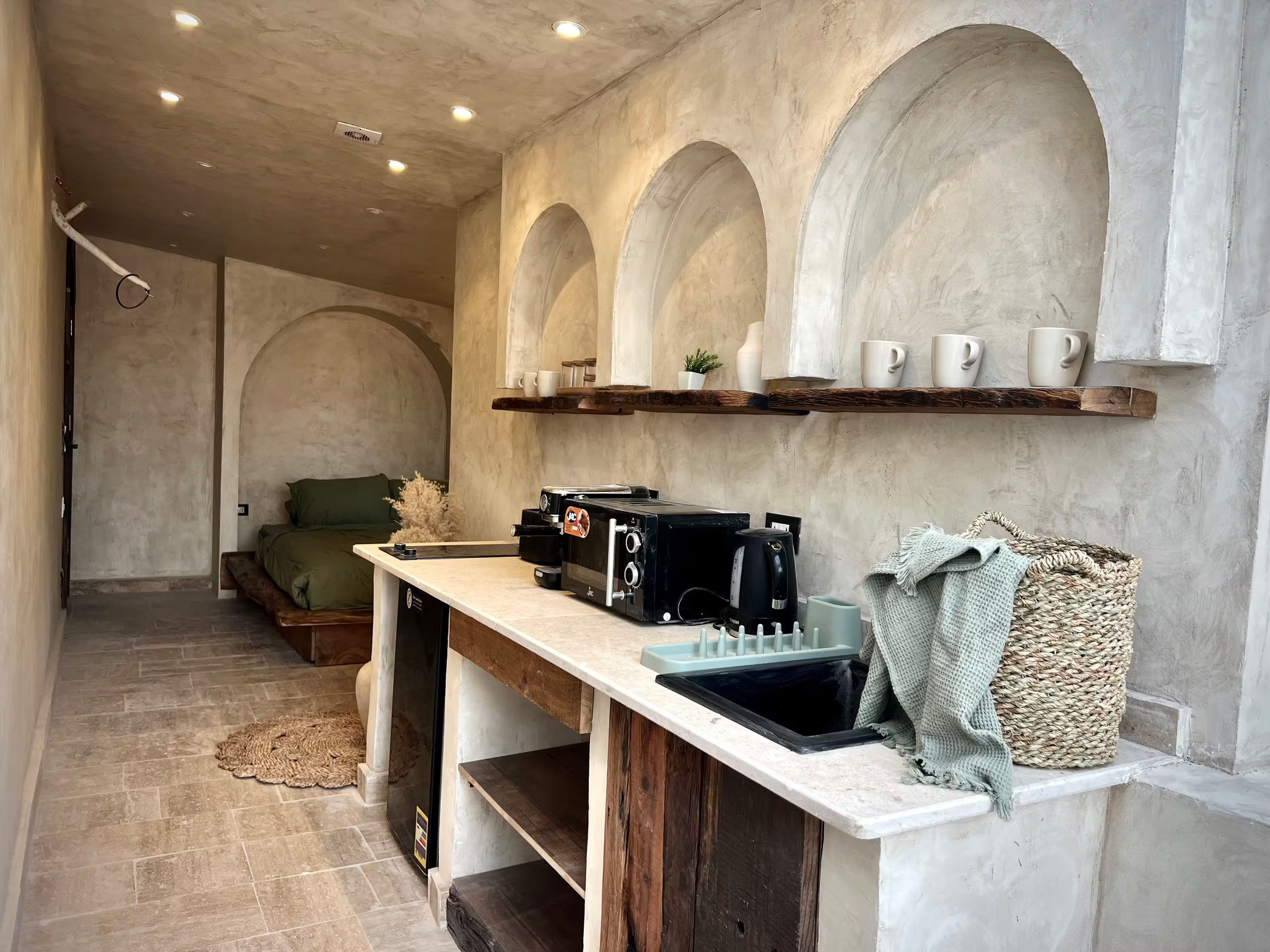 A compact kitchen with a built-in stove, a coffee machine, and a shelf with cups.