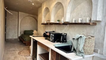 A compact kitchen with a built-in stove, a coffee machine, and a shelf with cups.
