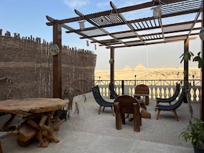 A wooden pergola with a view of the pyramids, a woven wall, and a rustic table. - Private Oasis Roof (Giza)