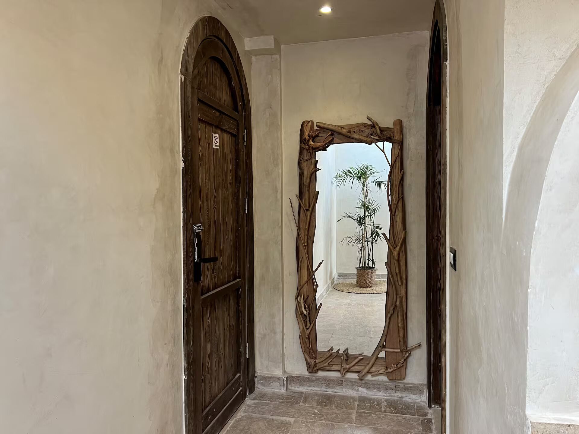A hallway with a wooden door and a rustic wooden archway leading to a room with a potted plant.