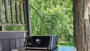 A Genesis portable grill in a covered outdoor area with a wooden deck and a tree.