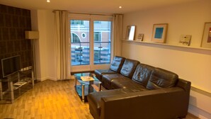 A modern living room with a leather sofa, a glass coffee table, and a TV on a stand. - 2-Bed 2-Bath Sea-View Balcony Apt inc Sun Terrace minutes to Sea, Station, Shops (Brighton and Hove)