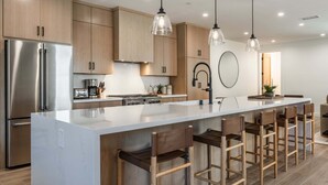 A modern kitchen with a large island, stainless steel appliances, wooden cabinets, and pendant lighting. - New Luxury 4BR /3BA Obsidian Reserve #88 – Private Hot Tub & Sauna, 2-Car Garage, gr8 Views! (Mammoth Lakes)
