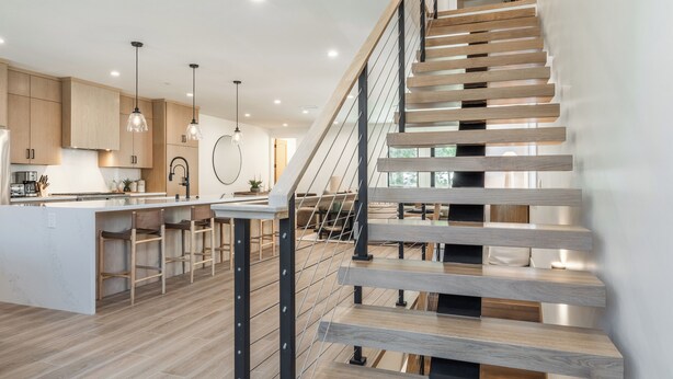 A modern kitchen with wooden cabinets, a central island with bar stools, and a staircase with wooden steps and metal railings. - New Luxury 4BR /3BA Obsidian Reserve #88 – Private Hot Tub & Sauna, 2-Car Garage, gr8 Views! (Mammoth Lakes)