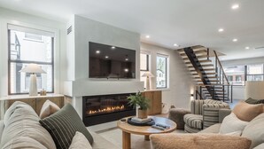 A modern living room with a fireplace, a flat-screen TV, and a staircase. - New Luxury 4BR /3BA Obsidian Reserve #88 – Private Hot Tub & Sauna, 2-Car Garage, gr8 Views! (Mammoth Lakes)