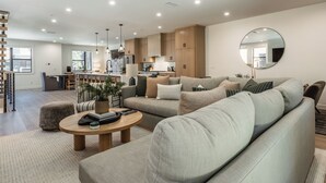 A modern living room with a sofa, coffee table, and a kitchen area in the background. - New Luxury 4BR /3BA Obsidian Reserve #88 – Private Hot Tub & Sauna, 2-Car Garage, gr8 Views! (Mammoth Lakes)