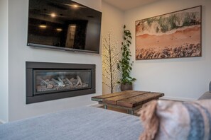 Moderni olohuone, jossa on takka, litteänäyttöinen televisio ja suuri maisemamaalaus.