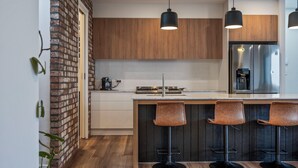 Une cuisine moderne avec des meubles en bois, un réfrigérateur en acier inoxydable et trois tabourets de bar.