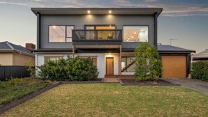 Une maison moderne à deux étages, dotée d’un balcon, de grandes fenêtres et d’une pelouse bien entretenue.