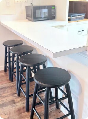 A kitchen with a white countertop, a black microwave, and three black stools.