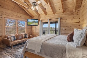 Ein Schlafzimmer einer Holzhütte mit Bett, Sofa, Deckenventilator und Fernseher.