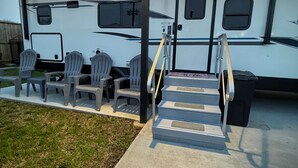 A covered outdoor area with a concrete staircase leading to a white RV with gray chairs and a table.