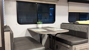 A compact RV interior with a kitchenette, a dining table, and seating areas.
