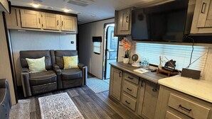 A compact RV interior with a kitchenette, a seating area with a sofa, and a small rug.