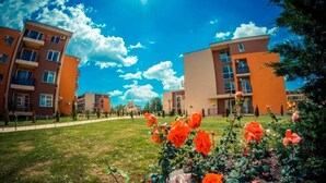 A residential building complex with multiple apartment buildings, a well-maintained lawn, and blooming flowers. - Pool View 2 Bed at Holiday Fort Club (Sunny Beach)