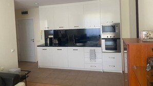 A compact kitchen with white cabinets, a black countertop, a built-in oven, and a microwave. - Pool View 2 Bed at Holiday Fort Club (Sunny Beach)