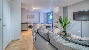 A modern living room with a grey sofa, a glass coffee table, and a TV mounted on the wall. - The Manchester City Haven (Manchester)