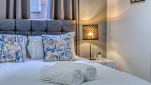 A neatly made bed with white linens, a headboard, and decorative pillows. - The Manchester City Haven (Manchester)