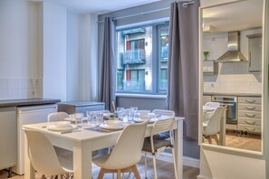 Eine moderne Küche mit weißen Schränken, einem Esstisch für vier Personen und einem großen Fenster mit Vorhängen.