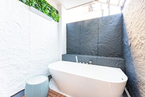 Une salle de bain moderne avec une baignoire sur pieds, un petit tabouret rond et un mur végétal.