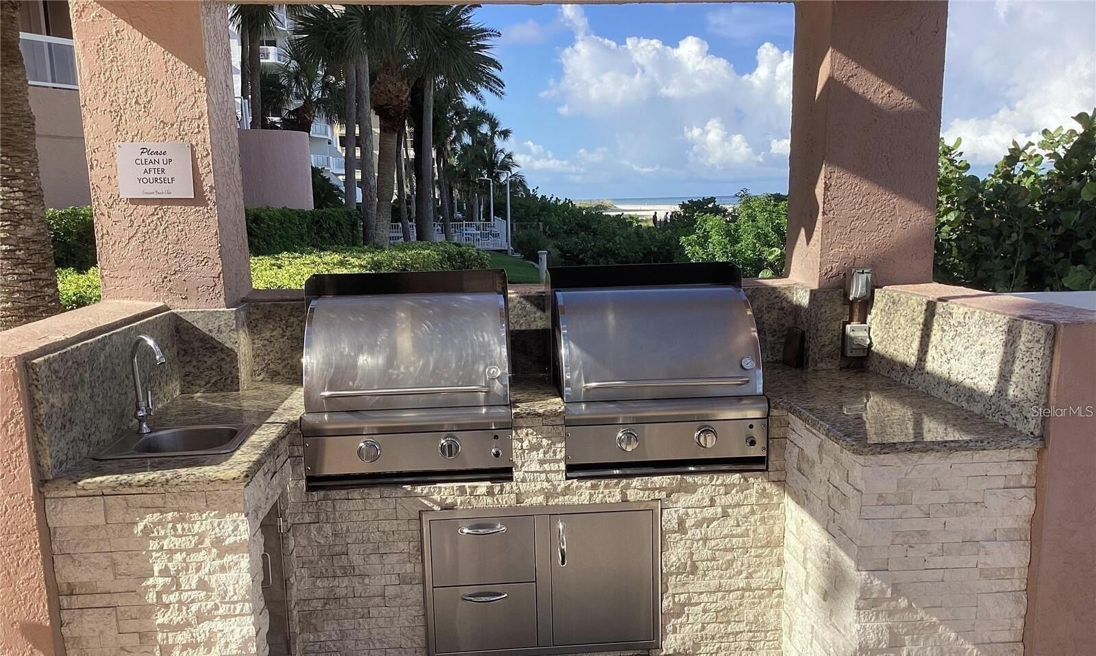 An outdoor kitchen with two stainless steel grills, a sink, and a storage cabinet.