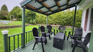 A covered outdoor seating area with chairs and a table, surrounded by a green deck and a stone wall. - ​Upstate Oasis: Moody Chic Interior & Summer Pool Fun (Carthage)