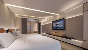 Une chambre d’hôtel moderne avec un grand lit, un téléviseur fixé au mur et une étagère intégrée.
