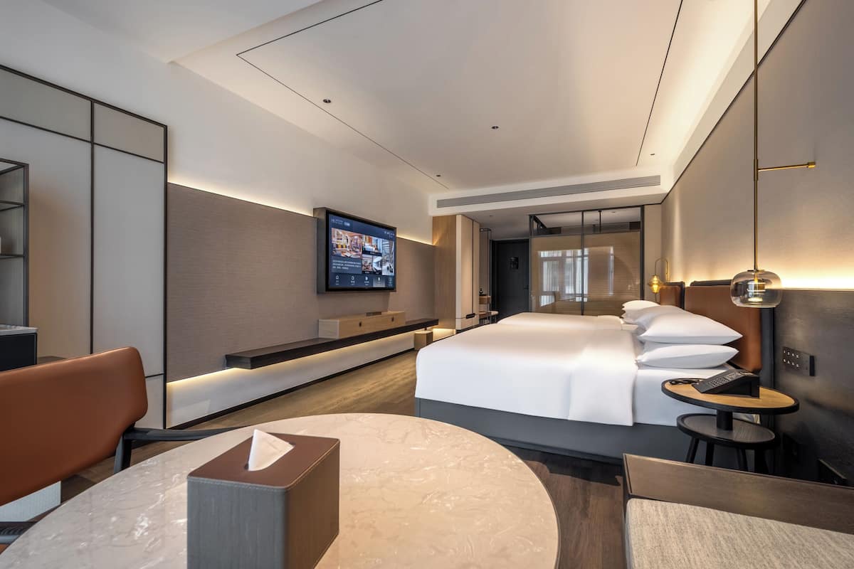 Une chambre d’hôtel moderne dotée d’un grand lit, d’un téléviseur fixé au mur, d’un bureau avec une chaise et d’une table ronde.