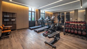 Een sportschool met loopbanden, een roeimachine en een dumbbellsrek.