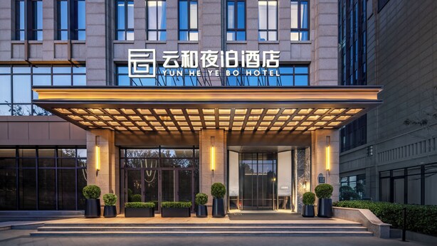 Een moderne hotelingang met een overdekte luifel, grote ramen en potplanten.