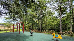 A playground with a red climbing structure, a green and blue seesaw, and a yellow and blue rocking horse. - Sandy`s Sanctuary - Conservation View - South-West Facing Pool (Davenport)