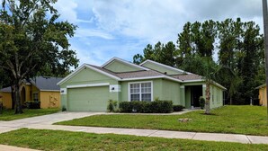A single-story house with a green garage, a front yard with grass and a sidewalk, and a tree to the left. - Sandy`s Sanctuary - Conservation View - South-West Facing Pool (Davenport)