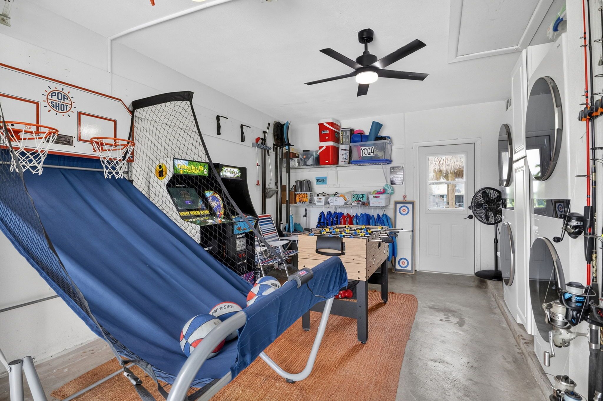 Une pièce avec un fauteuil bleu inclinable, un baby-foot, un ventilateur de plafond et un coin buanderie.